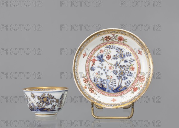 Bowl, house painter co-creator, Ferner, JF ca. 1750, or workshop house painter co-creator; Koenigliche Porzellain Fabrique, Meissen 1710–1763 factory/author. Hemispherical bowl with a rim at the bottom, parted, with a slightly rolled-up edge. Painted in cobalt in a Far Eastern motif with a bird and a rock decor by Fels und Vogel and with a polychrome house painter interior: a reclining man leaning against a rock, two floral compositions and an architectural motif in the circle of the bottom, around a cobalt branch. Floral decoration with a bird and a rock; cobalt semicircle pattern around the edge; flower in the bottom and bottom rim; gilded. Ca. mid-18th century. Meissen, Saxony, Germany. Vessel; height 4.5 cm, diameter 7.8 cm., A small porcelain cup and a matching saucer set against a plain gray background, the cup positioned to the left and the saucer on a brass stand to the right; both pieces are predominantly white with decorative blue floral motifs and accents of red and gold, th...