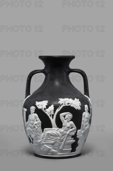 Portland Vase, copy, Josiah Wedgwood & Sons Stoke-on-Trent; pottery manufactory; 1790–1895. Pelike-shaped vase in black with white rendered from a black background reliefs depicting: 1 Atia, mother of Emperor Augustus, Apollo and Neptune; 2 Hecuba wife of Priam with a torch in her hand, surrounded by Venus and Paris. At the bottom, Paris, lost in thought. 19th/20th century, Staffordshire, Stoke-on-Trent, England. Vase; height 26.6 cm, width 19 cm., A dark vase with a matte black surface and two curved handles shows a raised white relief scene wrapping around its body; the relief depicts a reclining nude figure draped with cloth under a stylized tree, flanked by two standing partially draped figures and surrounded by architectural fragments and carved details. The colors visible are black, white, gray, and a few subtle variations of darker and lighter gray tones.