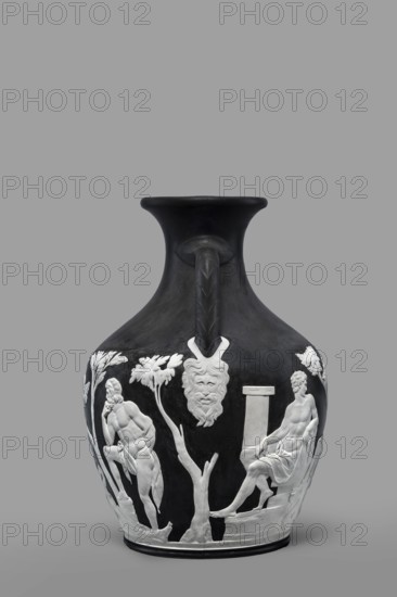 Portland Vase, copy, Josiah Wedgwood & Sons Stoke-on-Trent; pottery manufactory; 1790–1895. Maker: Josiah Wedgwood 1730–1795. Pelike-shaped vase in black with white reliefs rendered from a black background depicting: 1 Atia, mother of Emperor Augustus, Apollo and Neptune; 2 Hecuba wife of Priam with a torch in her hand, surrounded by Venus and Paris. At the bottom, Paris, lost in thought. 19th/20th century. Staffordshire, Stoke-on-Trent, England. Vase, height 26.6 cm, width 19 cm., A dark vase with a flared rim and a single curved handle rising from the neck features raised pale relief decoration around its body showing a group of classical figures and natural elements; a seated nude figure draped with cloth sits on a low support on one side while a standing muscular male figure leans on a tree or rock on the opposite side, both rendered in light color against the dark surface, accompanied by pale sculpted trees, foliage, a column-like element, and a stylized mask or face motif near th...