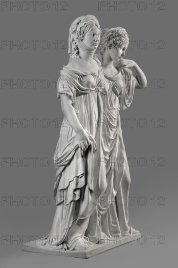 Two princesses, the so-called Prinzessinnengruppe, Koenigliche Porzellan Manufaktur KPM; Berlin; 1763–1918, sculptor Johann Gottfried Schadow 1764–1850. Double portraits of Luise von Mecklenburg-Strelitz 1776–1810 and Friedrich Friederike von Mecklenburg-Strelitz 1778–1841. On a flat rectangular base, two young women with their arms around each other in long, antique-style dresses made of thin fabric, draped under the bust Luise, wearing sandals, with curled, mid-length, center-parted hair. Luise puts her arm around her sister, resting her hand on her left shoulder; with her right lowered hand she supports the folds of her dress. Friederike embraces her sister from behind around the waist, her left hand grasping her sister's arm. Ca. 1795–1796, Berlin, Germany. Sculpture; height 55.0 cm, width 35 cm, depth 19.5 cm., A white marble sculpture of two women standing closely together on a rectangular base against a solid gray background, both wearing flowing draped garments with detailed fo...