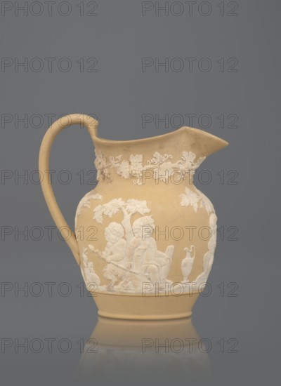 Oinochoe jug, cane ware pottery, beige-sand with a ribbon handle; around the belly, white reliefs: a group of three putti — two naked putti, tied with drapery, carry on a saddle a naked putto with a thyrsus and a vine; a naked putto with a panpipe is seated under a tree; a putto with two amphorae is seated under a tree; a satyr and a putto with two amphorae, a basket of vines; under the rim around the neck, a trail of vine shoots with fruit. Inside, a glazed jug. Maker: Wedgwood, Josiah 1730–1795; Etruria factory pottery manufactory. Date: c. 1815–1820. Place of manufacture: Stoke-on-Trent, Staffordshire, England. Subject: bacchanalia. Function: vessel. Height: 12 cm., A beige ceramic pitcher with a curved handle and a pointed spout, decorated with raised white reliefs depicting a group of cherubic figures, foliage, and a vase, set against a solid gray background; colors visible include beige, white, and gray.
