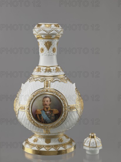 Bottle-shaped vase with a domed lid. Imperial Porcelain Factory in St. Petersburg 1744–1917; modeler: August Karlowicz Spiess 1817–1904. Embossed and colorfully painted decoration with four medallions against a rococo latticework: a miniature portrait of Tsar Alexander II in ceremonial military uniform with epaulettes and a blue ribbon, the Tsar's monogram, and the Tsar's double-headed eagle. Gilded floral and plant elements; a gap at the base and worn gilding. 1869, St. Petersburg, Russia. Porcelain vessel; height 49.5 cm, width 22 cm., A decorative porcelain vessel and its separate lid are shown against a plain gray background; the vessel is predominantly white with extensive gold ornamentation and includes a painted circular portrait on its bulbous body surrounded by a gilded frame, while the neck and foot feature raised white relief details and gilt accents; the separate lid echoes the same white and gold scheme with scalloped and beaded textures.