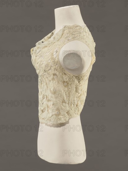 Bodice, lace, bodices, women's clothing, fashion. Pattern of rosettes connected by large spiders and heads; stylized floral motifs. 19th century, France. Clothing accessory. Height 36 cm; circumference 63 cm., A side view of a dress form torso displaying a sleeveless lace top in cream and pale yellow tones, with floral lace motifs and openwork patterns; the mannequin is off-white with a smooth matte surface, and the background is a uniform medium gray.