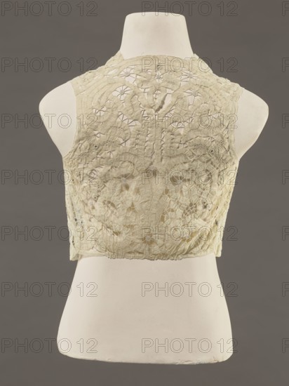 Bodice, lace, bodices, women's clothing, fashion. In a pattern of rosettes connected by large spiders and heads. Pattern of stylized floral motifs. 19th century, France. Clothing accessory. Height 36 cm, circumference 63 cm., A cream-colored lace sleeveless bodice displayed on a white mannequin torso against a dark gray background, showing an intricate floral and geometric lace pattern with openwork areas and raised embroidered motifs, scalloped edges at the shoulders and hem, subtle signs of wear and irregularities in the fabric, and visible texture contrasts between the delicate lace and the smooth mannequin surface; visible colors include cream, white, and dark gray.