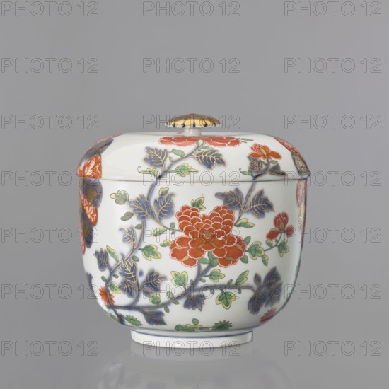 Vase lid with Imari decoration, Kaiserliche Porzellanmanufaktur in Wien 1744–1864. Imari style, Far Eastern-style floral decorations. Flat-arched lid with Imari decoration continued on the vase in a 4-part arrangement: two 6-petal brick-red cobalt half-rosettes with gilding, a lotus flower with leaves, and a peony flower on a branch, with a small bud. Flat gilded button-rosette handle, set on the lid in a cobalt band with a brick-red spiral. Mid-19th century; 18th century attribution noted. Austria, Vienna. Decorative vessel. Height 5 cm, diameter 21.5 cm. Maker: Praglowski, Jan fl. ca. 1954 attributed/inscription., A lidded ceramic jar displayed against a grey background, predominantly white with painted floral decoration in red, green, blue, and gold tones; the rounded body and domed lid show a repeated motif of stylized flowers and leaves, including a large red blossom on the front surrounded by green leaves and blue foliage outlined with gold; the lid has a small finial topped with...