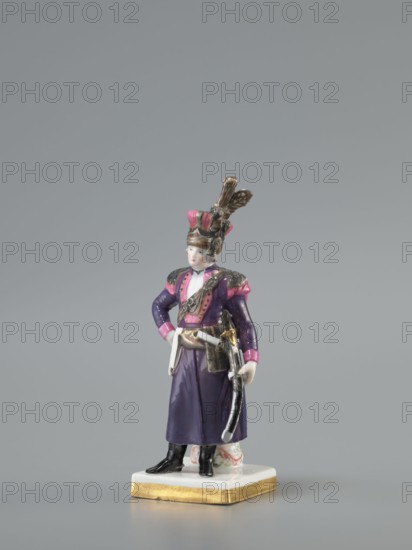 Figurine of an officer of the Polish Guard, Koenigliche Porzellain Fabrique, Meissen 1710–1763; figurine of a Polish guardsman. On a flat square base with gilded side edges, standing leaning against a low marbled column, a man in a purple kontusz with pink lapels, with epaulettes, a sabre strapped to the kontusz belt, a black map case, slung on a belt and leaning against the column at the back; on his head is a high pink cap with black decorations and a high broken tail placed at the side. Defined signature on the bottom of the base as a Galician noble guardsman, in the Austrian service. Dated to the 18th/19th century model marking with the letter K 1-100 from ca. 1791. Saxony; Meissen., A painted porcelain figurine of a standing person wearing a tall decorative hat with feather-like elements, a long purple coat with pink accents on the shoulders and cuffs, and black boots; the figure has a pale face and light-colored hair, a sash and belt with metallic-colored details, and a curved sw...