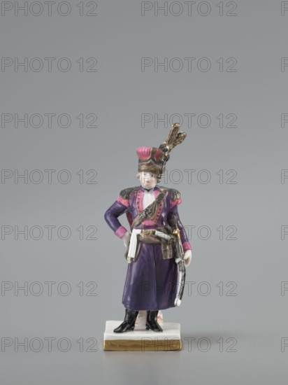 Figurine of an officer of the Polish Guard, Koenigliche Porzellain Fabrique, Meissen 1710–1763, figurine. On a flat square base with gilded side edges, standing leaning against a low marbled column, a man in a purple kontusz with pink lapels, with epaulettes, a sabre strapped to the kontusz belt, a black map case slung on a belt and leaning against the column at the back; on his head is a high pink cap with black decorations and a high broken tail placed at the side. Defined signature on the bottom of the base as a Galician noble guardsman, in the Austrian service. Dated to the 18th/19th century model marking with the letter K 1-100 from ca. 1791. Saxony; Meissen., A small porcelain figurine of a person wearing a tall hat with decorative feathers stands on a rectangular base with a gold-colored edge; the figure wears a purple coat with pink accents on the shoulders and cuffs, a white sash at the waist, black boots, and holds a curved object at the side, with visible colors including pu...