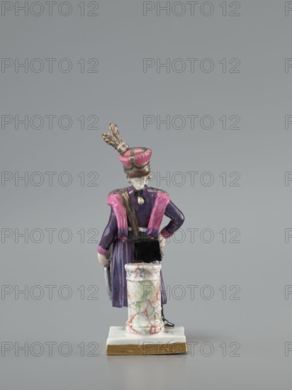 Figurine of an officer of the Polish Guard, Koenigliche Porzellain Fabrique, Meissen 1710–1763; porcelain figurine. On a flat square base with gilded side edges, standing leaning against a low marbled column, a man in a purple kontusz with pink lapels, with epaulettes, a sabre strapped to the kontusz belt, a black map case slung on a belt and leaning against the column at the back; on his head is a high pink cap with black decorations and a high broken tail placed at the side. Defined signature on the bottom of the base as a Galician noble guardsman, in the Austrian service. Dated to the 18th/19th century model/marking with the letter K 1-100 from ca. 1791. Saxony; Meissen., A small painted figurine viewed from behind standing on a square base with a gold edge, showing a person wearing a long purple coat with pink shoulder accents and matching pink cuffs, a pink and gold hat topped with gold feathers, and a white hair detail at the nape; the figure has one hand on the hip and the other...