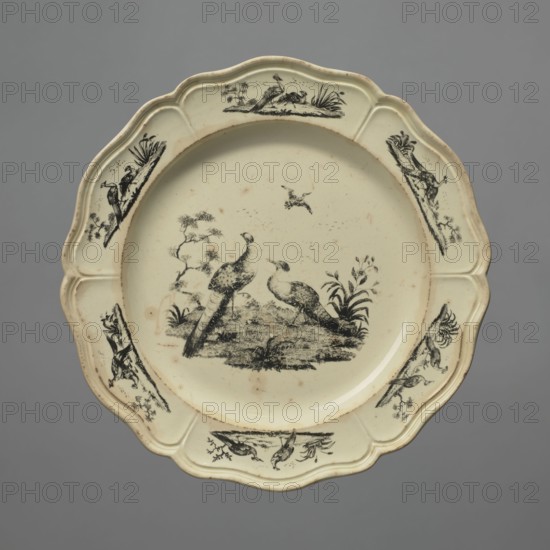 Plate with a pattern of Liverpool birds, Sadler & Green Liverpool, Josiah Wedgwood's Brick House Works, Derby Pot Works, peacocks, Liverpool birds, print, Wedgwood, Josiah 1730–1795. Plate with a 6-part collar with a Catherine relief around the edge and decoration in black print, a pattern of exotic Liverpool birds in the mirror and on six segments of the collar a peacock and pheasant motif in a summed landscape. c. 1765–1770, England, possibly Burslem or Derby. Earthenware plate, height 2.2 cm, diameter 24.0 cm., A scalloped ceramic plate with a pale cream surface and black decorative illustrations, featuring a central scene of two birds standing on a grassy mound surrounded by small plants, a few scattered marks on the surface, and a few smaller bird and foliage motifs arranged around the rim; the background is a solid gray.