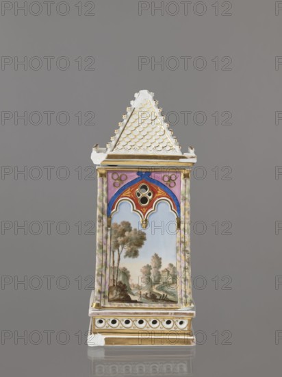 Night lamp by Alexander Popow porcelain manufacturer; 1806–1872. Neo-Gothic porcelain lamp, composed of three parts: base, lamp, and cover. Base has a horizontal row of holes on each side forming a decorative trail. Cube-shaped lamp in neo-Gothic style with arcades shaped like tracery, painted with colorful landscapes: two with motifs of flowering bushes primrose and jasmine, floral motifs against a landscape background, and two landscapes with an architectural motif. 19th century, Gorbunovo, Russia. Height 32.2 cm, width 13 cm., A tall, narrow porcelain object shaped like a small tower with a steep, textured roof in white and gold sits against a gray background; the upper roof section has a scalloped pattern in white highlighted with gold, and gold trim appears below it. The tower's central panel features a painted pastoral scene with a blue sky, green and brown trees, and buildings in muted earth tones, framed by decorative arches in red, blue, pink, and gold; the sides of the panel ...