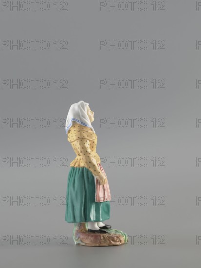 Figurine: Peasant Woman, Popov, Alexander porcelain factory; 1806–1872 — porcelain figurine depicting a woman in a white scarf with a blue border on her head, wearing a green skirt and apron with red stripes, and a yellowish caftan with black dots. Base missing. Circa 1830–1840, Gorbunovo, Russia. Height 3.5 cm; width 6.0 cm; depth 5.7 cm., A small ceramic figurine of a woman standing on an irregular base, wearing a white headscarf with a blue edge, a yellow blouse with a subtle dotted pattern, a green skirt, a striped apron in red and white tones, white stockings, and black shoes; the base shows muted earth tones and a touch of green, and the background is a uniform gray.