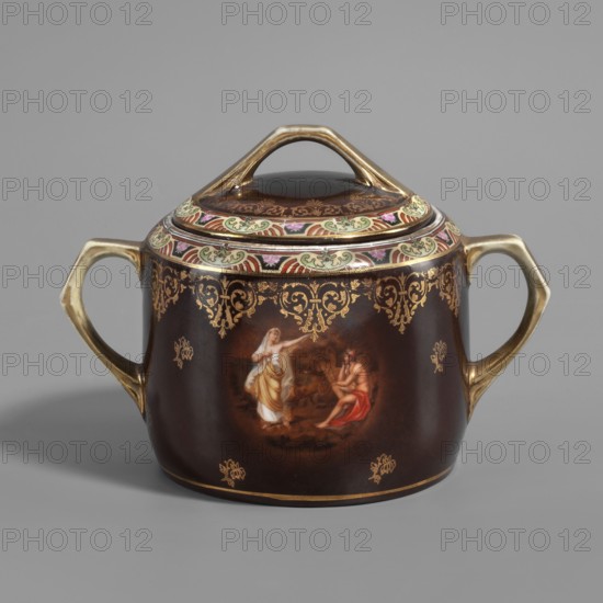 Sugar bowl with lid from a tea service set. Cylindrical sugar bowl with slatted handles, double-folded on the outside, with a recessed flat lid with a tripartite slatted handle. Brown-chocolate body with a colourful ornament featuring a stylised palmette motif and a gilding trail of leafy volute-palmette styles around the edges. On the side, a colourful miniature with an antique-style scene: a seated naked man wearing a crown, with a red drapery draped over his hip, and a woman in a light robe standing next to him with her left hand outstretched. Small golden flower sprigs on the brown belly; handles and lid handle gilded. Imitation, gilding, mythological subject. Early 20th century. Possibly Vienna or Czech Republic. Vessel; height 11 cm, width 10.5 cm, depth 16 cm., A brown ceramic lidded container with two gold-toned handles and a matching arched gold-toned lid handle sits on a gray surface against a gray background; the body and lid feature ornate gold scrollwork and decorative mot...