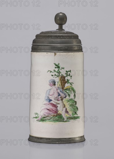 Cylindrical tankard in a pewter frame, Prószków Slaski faience factory; 1763–1853. White, painted in colors. From the front, a depiction of a barefoot woman sitting under a tree, her blouse unbuttoned, revealing her breasts. The woman, head turned to the right, supports with her right hand a small child, dressed in a short T-shirt, running towards her from the left. It can be interpreted as an allegorical representation of Maternitas motherhood. The representation is painted with some freedom. Late 18th century, Silesia Province of Silesia. Vessel; height 24.0 cm, width 15.0 cm, depth 10.5 cm., A tall cylindrical ceramic tankard with a rounded metal lid and finial, the lid and base are a dark metallic gray and the ceramic body is an off-white or cream color; on the front of the body is a painted scene showing a seated woman with pale skin and light bluish-gray hair wearing a blue top and a pink skirt, a small child with pale skin and light-colored hair reaches up toward her while leani...