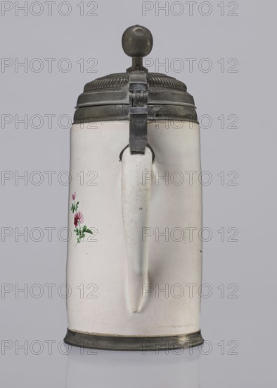 Cylindrical tankard in a pewter frame, Prószków Slaski faience factory; 1763–1853. Cylindrical tankard in a pewter frame. White faience, painted in colors. From the front: a barefoot woman sitting under a tree, her blouse unbuttoned revealing her breasts; her head turned to the right as she supports with her right hand a small child, dressed in a short T-shirt, running towards her from the left—interpreted as an allegorical representation of Maternitas motherhood. The representation is painted with some freedom. Late 18th century. Province of Silesia 1742–1918, Silesia, Prószków Slaski. Vessel. Height 24.0 cm; width 15.0 cm; depth 10.5 cm., A white ceramic tankard with a curved handle and a metal hinged lid topped by a round metal knob, the tankard showing small painted floral decoration in green and red on one side; the metal lid and base are dark gray, the background is light gray, and the ceramic surface has subtle off-white and slightly speckled areas.
