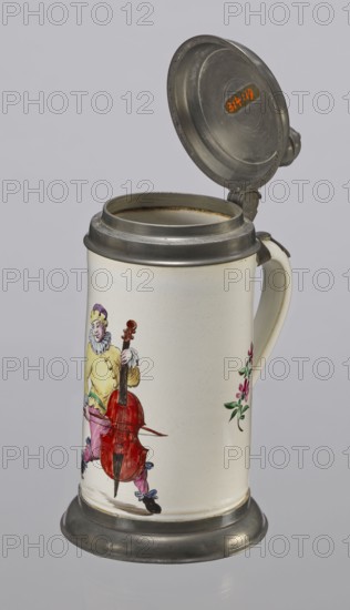Tin-mounted tankard, Prószków Slaski faience factory 1763–1853. White cylindrical tankard in a pewter mount. On the front is a depiction of an obese musician playing a double bass, shown in vigorous movement. The musician wears a yellow jacket, purple pantaloons, and a lilac hat with a yellow brim. Floral sprigs on the sides. Pewter cover engraved CGH/1811. Late 18th century. Silesia Province of Silesia, 1742–1918, Prószków Slaski. Vessel. Height 24.0 cm; width 15.0 cm; depth 9.5 cm., A ceramic tankard with a hinged metal lid and metal base, shown open to reveal the interior rim, with a curved handle on the side; the body of the tankard is off-white with painted decorations including a figure in colorful clothing holding a large red stringed instrument and a small spray of pink and green flowers on the adjacent side; the metal parts are gray and the painted figure includes yellow, purple, pink, red, blue, green, black, and skin-tone hues.