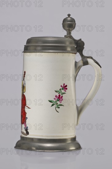 Tin-mounted tankard, Prószków Slaski faience factory 1763–1853. White cylindrical tankard in a pewter mount. On the front is a depiction of an obese musician playing a double bass, shown in vigorous movement; the musician wears a yellow jacket, purple pantaloons, and a lilac hat with a yellow brim. Floral sprigs on the sides. Tin cover engraved CGH/1811. Late 18th century. Province of Silesia 1742–1918, Prószków Slaski. Vessel; height 24.0 cm, width 15.0 cm, depth 9.5 cm., A ceramic stein with a metal hinged lid and metal base visible against a pale gray background, the stein body is off-white with a glossy finish and small speckling, a painted floral motif in shades of pink and green appears on one side, a portion of a painted figure in red and brown is partially visible, the handle is off-white with metal fittings at the top, the metal lid and base are dull silver-gray with a slightly tarnished appearance, and the overall scene shows a few colors including off-white, silver-gray, pin...