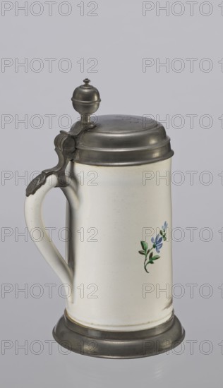 Tin-mounted tankard, Prószków Slaski faience factory 1763–1853. White cylindrical tankard in a pewter mount. On the front is a depiction of an obese musician playing a double bass, shown in vigorous movement. The musician is dressed in a yellow jacket, purple pantaloons, and a lilac hat with a yellow brim. Floral sprigs on the sides. On the tin cover engraved CGH/1811. Late 18th century. Silesia Province of Silesia, 1742–1918. Prószków Slaski. Vessel. Height 24.0 cm; width 15.0 cm; depth 9.5 cm., A light-colored ceramic stein with a curved handle and a metal hinged lid topped by a rounded finial, the stein has metal accents at the lid and base and a small floral motif with green leaves and blue petals on its body; visible colors include white, gray, silver, green, and blue.