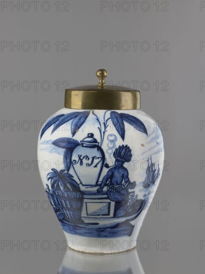 Tobacco jar with brass lid, De Vergulde Blompot faience factory; 1616–1841; Delft ceramics centre; ca. 1600– . Ovoid vase with a low, slightly parted neck. White tin-glazed faience painted in cobalt with a genre scene depicting an Indian smoking a pipe under a tobacco bush and a vase with the number No. 17. The scene is set against a schematic seascape with two sailing ships. An Indian sits on a pedestal on which stands an ovoid vase with a lid; on the opposite side of the pedestal sits a basket with a pineapple and a container for liquid. Similar vessels serving as tobacco jars were produced in the Netherlands throughout the 18th century. The inscriptions on the vase standing on the pedestal referred either to the origin or the type of tobacco. 18th century, Delft, Netherlands. Vessel: height 25 cm; width 21.5 cm. Lid: height 7.6 cm; width 12.8 cm., A rounded ceramic jar with a domed metallic lid topped by a small knob sits against a neutral gray background; the jar has a white base c...