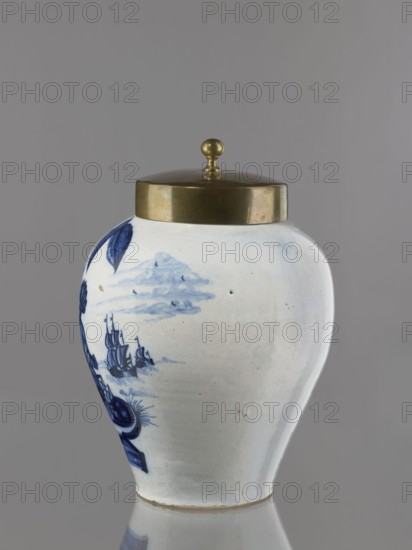 Tobacco jar with brass lid. De Vergulde Blompot faience factory, 1616–1841; Delft ceramics centre, ca. 1600– . Ovoid vase with a low, slightly parted neck. White tin-glazed earthenware painted in cobalt with a genre scene depicting an Indian smoking a pipe under a tobacco bush and a vase labeled No. 17. Scene set against a schematic seascape with two sailing ships. An Indian sits on a pedestal supporting an ovoid vase with a lid; on the opposite side of the pedestal is a basket with a pineapple and a liquid container. Similar tobacco jars were produced in the Netherlands throughout the 18th century. The inscriptions on the vase on the pedestal refer either to the origin or the type of tobacco. 18th century, Netherlands; Delft. Vessel. Height 25 cm; width 21.5 cm. Lid: height 7.6 cm; width 12.8 cm., A ceramic jar with a rounded vase shape and a metallic lid with a small round knob is shown against a neutral gray background; the jar is primarily white with blue painted decorations includ...