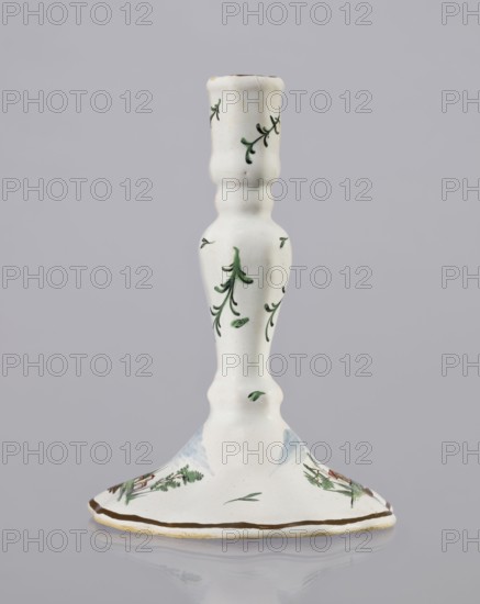 Candlestick, Prószków Slaski faience factory active 1763–1853. Candlestick in the shape of a polygonal baluster supported on a wide, round conical base with a wavy edge. Painted colorfully; on the foot are two miniatures depicting landscapes with architecture and oblique projections of twigs on the shaft. Late 18th century, circa 1770–1783. Silesia Province of Silesia. Prószków Slaski. Candlestick; height 18.2 cm, width 13.0 cm., A white ceramic candlestick with a tall, slender, turned shape and a flared base, decorated with small green leafy sprigs and simple painted foliage; the base shows additional hand-painted green and brown landscape-like motifs and a thin brown rim, and the overall colors visible are white, green, brown, and a touch of pale blue.