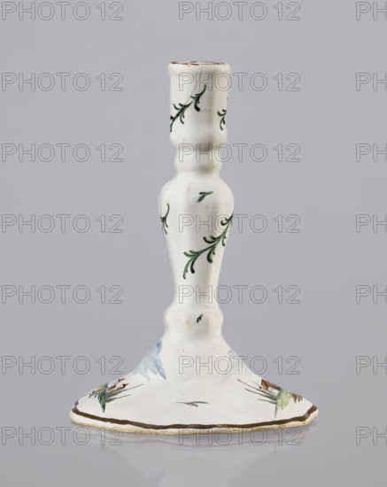 Candlestick, Prószków Slaski faience factory; 1763–1853. Candlestick in the shape of a polygonal baluster supported on a wide, round conical base with a wavy edge. Painted colorfully. On the foot are two miniatures with a landscape with architecture; oblique projections of twigs on the shaft. Candlestick, 1770–1783. Province of Silesia, Prószków Slaski, Silesia. Height 18.2 cm; width 13.0 cm., A white ceramic candlestick with a turned, curving stem and a flared base, decorated with small green leafy vine motifs and a few brushstrokes of blue and green on the base; the rim and edge have a thin brown accent, and the surface shows subtle speckling and a glossy finish against a neutral gray background.