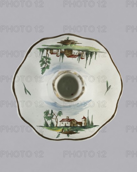 Candlestick, Prószków Slaski faience factory 1763–1853. Candlestick in the shape of a polygonal baluster supported on a wide, round conical base with a wavy edge. Painted in color; on the foot are two landscape miniatures with architecture and oblique projections of twigs on the shaft. Circa 1770–1783. Manufacture: Prószków Slaski, Silesia Province of Silesia. Height 18.2 cm; width 13.0 cm., A scalloped ceramic dish with a central cylindrical holder sits against a pale gray background; the dish is primarily white with a thin brown rim and features painted small landscape scenes in green, brown, red, and blue. The visible decoration includes a group of building shapes with red roofs and brown walls set among green trees and grassy areas, mirrored near the top and bottom edges of the dish, along with a few slender green leaf-like strokes elsewhere; soft blue brushstrokes suggest sky around the central holder.