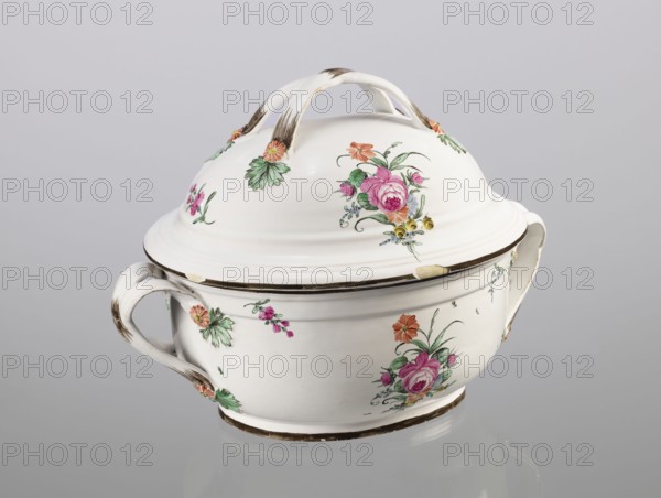Vase with lid, Prószków Slaski faience factory 1763–1853, egg-shaped soup tureen with a lid in the form of a flattened ellipsoid/hemisphere. Handles of the vase and lid are two crossed ribbons. Decorated with small painted floral projections and large bouquets of multicolored flowers; on both sides of the vase and lid are bouquets with a pink rose. Handles are adorned with vermilion daisies with large green leaves. Rim of the vase and cover painted brown. Ca. 1785, Province of Silesia Silesia, Prószków Slaski. Vessel; height 25.5 cm, length 35.5 cm., A lidded ceramic tureen with a glossy white surface sits against a pale gray background, featuring a curved handle on each side and an arched double handle on the domed lid; the piece is decorated with painted floral motifs in pink, green, orange, yellow, and touches of blue, and shows areas of brownish discoloration or wear along the handles and rims.