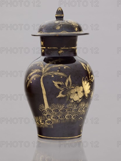 Kuan-type vase with cover, faience manufactory 1779–1800. Maker: Karol Wolff fl. ca. 1800. Chinoiserie; Chinese/Far Eastern motifs; Warsaw faience; unknown provenance. Low kuan-type vase in the shape of a bulging baluster with a cylindrical neck and a low domed cover with an acorn-shaped handle. Against a chocolate background a gold-painted garden fragment with two chrysanthemum bushes, a peony bush, a palm tree, a rice fence, and between them the figure of a Chinese man with a bag and a walking stick. Around the neck is a thin simple plant twig; a painted flowered branch on the lid. Late 18th century. Warsaw, Poland. Vessel: height 19.5 cm, diameter 13.5 cm; lid: height 7.5 cm, diameter 10.5 cm., A dark vase with a lid sits against a pale gray background; the vase is predominantly deep black or very dark brown with decorative gilded designs in gold, including floral motifs, leaves, a palm-like tree, and curving ornamental patterns; the lid shares the dark base color and gold embellish...