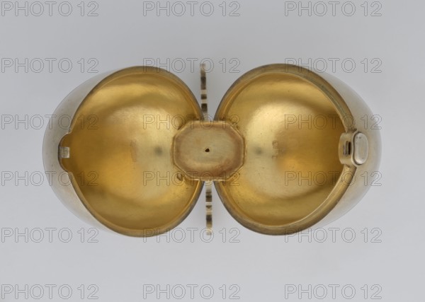 Easter egg, lilies of the valley, flowers, Easter eggs, silver egg, smooth, composed of two opening halves on a hinge, cut vertically; on one part an enameled bouquet of forget-me-nots; gilded interior with an octagonal basket for embedding a surprise missing. Egg supported on a four-legged stand, 1890s, St. Petersburg, decorative object. Dimensions: height 11.4 cm, width 6.6 cm, depth 6.6 cm; weight 233.5 g., A symmetrical overhead view of a metallic object opened to reveal two rounded interior halves with a central raised connector, showing a reflective gold-colored interior and a silver-colored exterior, set against a light gray background.