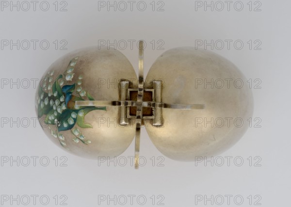 Easter egg, lilies of the valley and forget-me-nots motifs, silver egg, smooth, composed of two opening halves on a hinge, cut vertically; one part with an enameled bouquet of forget-me-nots; gilded interior with an octagonal basket for embedding a surprise missing. Egg supported on a four-legged stand. 1890s, St. Petersburg. Decorative object. Height 11.4 cm, width 6.6 cm, depth 6.6 cm, weight 233.5 g., A pair of round metallic objects joined at the center by a cross-shaped metal fixture sit against a pale background; the metal surfaces are primarily muted gold and silver tones with areas of darker patina, and one of the rounded forms bears a painted floral motif in shades of green and blue with small pale blossoms.