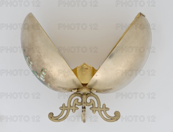 Easter egg, lilies of the valley, flowers; Easter egg, silver, smooth, composed of two opening halves on a hinge, cut vertically; one part with an enameled bouquet of forget-me-nots; gilded interior with an octagonal basket for embedding a missing surprise. Egg supported on a four-legged stand; 1890s, St. Petersburg; decorative object. Height 11.4 cm, width 6.6 cm, depth 6.6 cm, weight 233.5 g., A decorative metal object with a pair of large, curved, shell-like halves opened upward, mounted on an ornate base with scrolling, symmetrical supports; the metal surfaces show a pale gold to silvery patina with areas of darker toning and a few small green painted floral motifs on one inner curved panel; the base and interior edges display a warmer golden tone, and the background is a neutral light gray.
