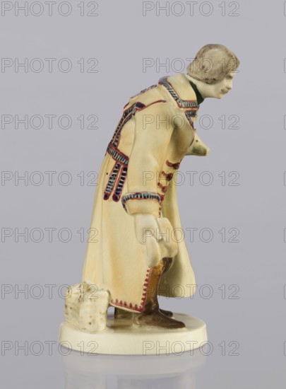Peasant with Piglet, First Galician Factory of Artistic Faience and Terracotta Pacyków; 1912–1939 manufacturer, Popiel, Antoni 1865–1910 sculptor, figurine of a man in peasant Hutsul russet coat on a circular base. The peasant, with straight-cut hair and period mustache, stands slightly bowed, holding a hat in his right hand and a piglet under his left arm. At the back, on the base, a woven basket. Warm tones, the light ochre of the russet coat accentuated by brown-purple trim; underneath, a green vest, dark trousers and brown shoes. Ca. 1910, Pacyków; terracotta/faience figurine; height 14.5 cm, width 8.0 cm, depth 5.5 cm., A ceramic figure of a person leaning forward wearing a long coat in cream with decorative trim in blue and red, a green collar, brown shoes, and a beige and gray hair/hat area, standing on a cream round base next to a small cream parcel with mottled brown marks, all set against a light gray background.