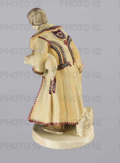 Peasant with Piglet, First Galician Factory of Artistic Faience and Terracotta Pacyków; 1912–1939 manufacturer, Popiel, Antoni 1865–1910 sculptor. Figurine of a man in a peasant Hutsul russet coat on a circular base. The peasant, with straight-cut hair and a period mustache, stands slightly bowed, holding a hat in his right hand and a piglet under his left arm. A woven basket is on the base at the back. Warm tones: light ochre russet coat with brown-purple trim; underneath a green vest, dark trousers, and brown shoes. ca. 1910. Pacyków. Terracotta figurine. Height 14.5 cm; width 8.0 cm; depth 5.5 cm., A ceramic figurine viewed from behind showing a person wearing a long coat with decorative trim, holding a small animal under one arm and standing on an oval base; the coat is primarily pale yellow with red and dark blue decorative accents, the small animal and base are off-white, the person's hair is a muted brown, and there are subtle brown and beige tones on the figure and base.
