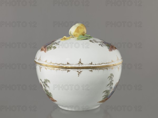 Punch vase with lid, Königliche Porzellan-Manufaktur KPM, Berlin; 1763–1918 maker marking; porcelain with reliefs and enamel genre miniatures. Hemispherical bowl with bottom rim and arched circular lid topped by a plastic half-peeled lemon with stem, leaf, two slices and rolled-up peel. Rim of vase and lid with gilded relief rocaille decoration. Two color miniatures each on bowl and lid after engravings by W. Hogarth?: on the lid—1 three men in 18th-century costume seated at a table with a vase and glasses, 2 three men at a table with a vase, one standing; on the bowl—1 six people seated at a round table with glasses and pipes, one figure reclining in front of the table, 2 seven people seated at a table singing, smoking pipes and conversing. Late 4th quarter of the 18th century late 18th century, Berlin, Germany. Vase; height 27.5 cm, width 28 cm., A rounded white porcelain lidded container with a glossy finish sits against a gray background; the lid has a sculpted yellow fruit with gr...