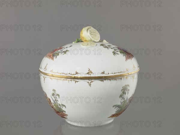 Punch vase with lid, Koenigliche Porzellan Manufaktur KPM; Berlin; 1763–1918. Porcelain, reliefs and colour genre miniatures. Hemispherical bowl with bottom rim, arched circular lid with handle modeled as half a peeled lemon with stem, leaf, two slices and rolled-up peel. Rim of vase and lid with gilded relief rocaille decoration. Two painted miniatures on bowl and two on lid after engravings by W. Hogarth?: lid—park scenes: 1 three men in 18th-century costume seated at a table with a vase and glasses; 2 three men at a table, one standing. Bowl—park scenes: 1 six people at a round table with glasses and pipes, one reclining before the table; 2 seven people at a table, singing, smoking pipes and conversing. 4th quarter of the 18th century, Berlin, Germany. Vase: height 27.5 cm; width 28 cm., A rounded white ceramic covered bowl sits centered against a neutral gray background, the lid topped with sculpted lemon halves and a small green stem in pale yellow and green tones. The bowl and li...