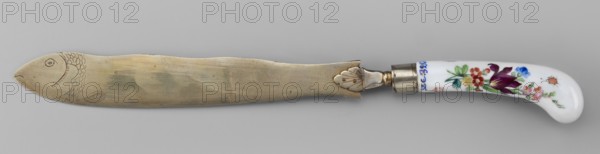 Knife, Korzec Porcelain and Faience Manufactory; 1790–1832. Possibly a Korzec forgery. Cutlery with a white-metal blade featuring a palmette at the base of the handle and an engraved fish at the end of the blade. Slightly curved porcelain handle with colorful painted flower bouquets and insects on both sides. Circa 1830. Poland Korzec?. Height 30 cm., A long flat metal blade with a rounded end engraved with a fish head and scale-like markings lies horizontally above a pale gray background, its metal showing a muted golden-silver patina with subtle uneven shading and a few small marks; the blade connects to a metal ferrule with a decorative leaf-shaped mounting and a short collar, which joins a curved glossy white handle painted with colorful floral motifs in shades of purple, red, pink, blue, green, and a small orange detail.