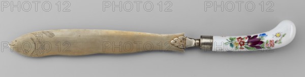 Knife, ca. 1830. Porcelain and faience manufactory work Korzec, 1790–1832; possible Korzec forgery. Cutlery knife with slightly curved porcelain handle painted with colorful flower bouquets and insects on both sides. Blade made of white metal with a palmette at the base of the handle and an engraved fish at the end of the blade. Height 30 cm. Country of origin: Poland., A long knife with a dull metallic blade that has an etched fish head and scale pattern near one end, attached to a curved white handle decorated with painted floral motifs; the blade shows a warm muted metallic color while the handle features colors including white, purple, red, pink, green, yellow, blue, and a small amount of metallic silver where the ferrule connects the blade and handle.