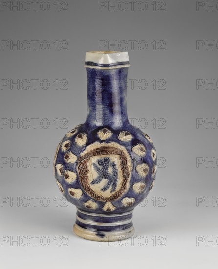 Jug, Westerwald ceramics center; ca. 1400–, stoneware jug with spherical body, high cylindrical neck and small triangular spout; wide almost cylindrical foot profiled with transverse rims and widened by a roller at the base; prominent U-shaped applied handle. Glazed in grey and cobalt blue with manganese accents. Relief decoration: three oval medallions within a wreath of radially arranged stylized lilies on the body. Central medallion: coat of arms with a crowned griffin; side medallions: busts of Louis XIV. Each medallion is surrounded by a ribbon inscribed LUDOVICUS XIII.FRANCIAE.ET.N.REX.CHR.1679 and a laurel wreath. Below the medallions a symmetrical floral composition includes French lilies and the letters PR. Belly background is sapphire except for a wide vertical stripe at the back, Louis's hair, the background of the ribbons and plant frames of the medallions, and the centers of the lilies, which are cherry-brown. Late 17th–18th century, Germany. Vessel; height 27.5 cm, width ...