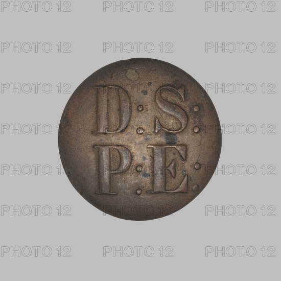 Uniform button, Biertümpfel, Frederick fl. 1832–1870 manufacturer, button maker, monograms, round slightly convex uniform button, shank broken off; obverse inscribed D:S:/P:E.; reverse in rim stamped F. BIERTUMPFEL / in WARSAW / No. 460 and in Cyrillic 1oj sort; late 19th century, Warsaw, Poland; clothing accessory, diameter 2.5 cm., A round metal object with a weathered surface sits against a plain light gray background; the object shows a patina of brown and dark brown with some darker spots and small greenish corrosion marks, and its surface has shallow raised shapes and round depressions.