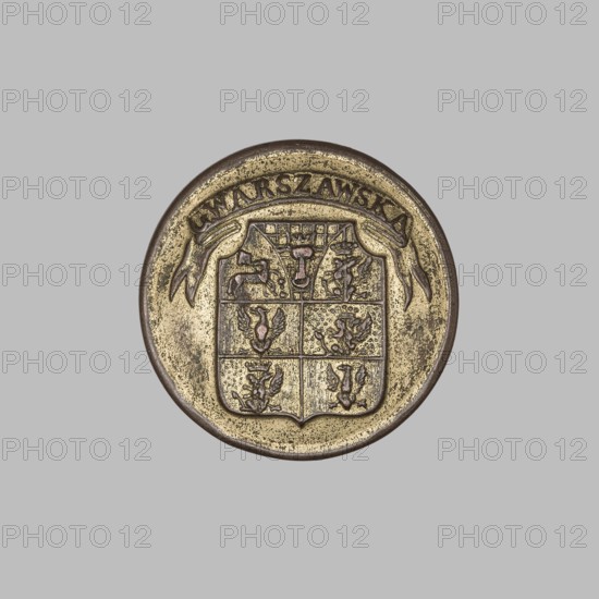 Button from an official's uniform, maker: Münchheimer, Zygmunt the Younger 1787–1875, fl. 1816–ca. 1870. Clothing accessory, diameter 2.1 cm. Obverse: multi-field coat of arms of the Warsaw Governorate 1845–1866 with the inscription on the sash GWARSZAWSKA. Reverse: strongly faded company name. Date: 1845–1866. Place of origin: Warsaw, Poland., A round metallic medallion with a worn surface set against a plain light gray background; the medallion shows a bordered shield divided into sections with small raised decorative figures and a ribbon-like banner arcing above it; visible colors include gold, brass, bronze, brown, and grayish tones across the metal with darker brown in the recessed areas.