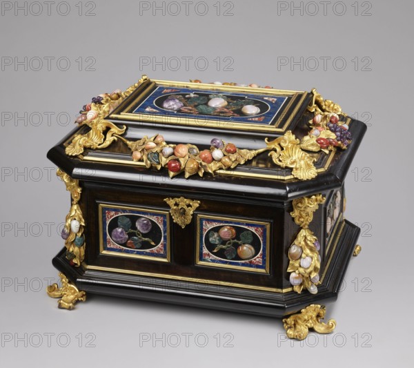 Jewel box, pietra dura technique. Jewel box made of blackened wood, partly ebony, cuboid with chamfered corners supported on four gilded bronze volute legs decorated with a mascaron at the base; the edge of the base and the edge of the lid with profiled ebony strips. Decorated on the side walls with six mosaic reserves and one plaque on the lid: front and back two panels with two fruits on a branch; sides one panel each with three fruits on a branch and an insect at the bottom. Corners with cast gilded bronze garlands topped with medusa masks and plastic fruits of semi-precious stones 7 pieces each. Hinged, profiled lid with a large plate showing three fruits on branches tied with a sash, an insect at the top; side walls with gilded bronze garlands with plastic fruits; corners with gilded bronze shells; front with a preserved key hole. Dated to the early 18th century early 18th century, Florence?, Italy?. Chest; height 34.5 cm, width 41.5 cm, depth 50.5 cm., A decorative rectangular bo...
