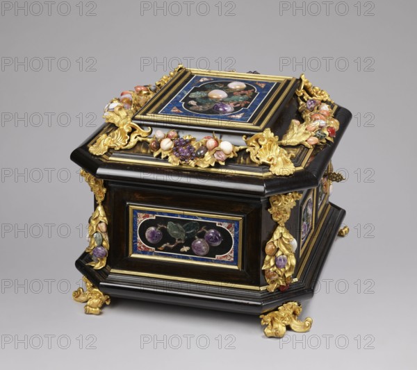 Jewel box, pietra dura technique. Made of blackened wood, partly ebony, cuboid with chamfered corners supported on four gilded bronze volute legs decorated with a mascaron at the base. The edge of the base and the edge of the lid have profiled ebony strips. Decorated on the side walls with six mosaic reserves and one plaque on the lid: front and back panels show two fruits on a branch; side panels show three fruits on a branch with an insect at the bottom. Corners have cast gilded bronze garlands topped with Medusa masks and plastic fruits made of semi-precious stones 7 pieces each. The hinged, profiled lid has a large plate with three fruits on branches tied with a sash and an insect above; side walls bear gilded bronze garlands with plastic fruits; corners feature gilded bronze shells; front has a preserved keyhole. Dated to the early 18th century, likely Florence, Italy. Chest; height 34.5 cm, width 41.5 cm, depth 50.5 cm., A decorative box with a dark wood finish and gold ornamenta...