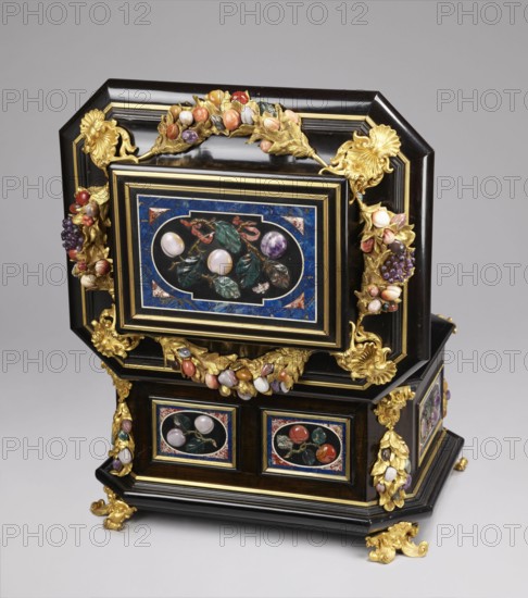 Jewel box, pietra dura; made of blackened wood, partly ebony, cuboid with chamfered corners supported on four gilded bronze volute legs decorated with a mascaron at the base. The edge of the base and the edge of the lid have profiled ebony strips. Decorated on the side walls with six mosaic reserves and one plaque on the lid. Front and back panels show two fruits on a branch; side panels show three fruits on a branch and an insect at the bottom. Corners feature cast gilded bronze garlands topped with medusa masks and plastic fruits made of semi-precious stones 7 pieces each. Hinged, profiled lid decorated with a large plate with three fruits on branches tied with a sash, with an insect above; side walls with gilded bronze garlands with plastic fruits; corners with gilded bronze shells; front retains a keyhole. Dated to the early 18th century 18th century, likely Florence, Italy. Dimensions: height 34.5 cm, width 41.5 cm, depth 50.5 cm., A decorative box with a dark brown or black woode...