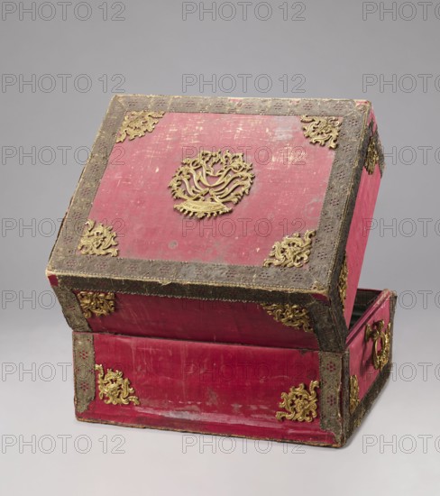 Casket case, The case is a rectangular wooden box covered with red velvet, with gold thread trimmings on the edges. The crosspieces have bronze openwork overlays. The side walls have gilded bronze handles; the top has a decorative overlay in the middle with a rank crown. On the front wall is a decorative overlay serving as a lock plate; the keyhole is preserved. The interior is lined with light green silk. Early 19th century; 18th century, Italy possibly Florence. Chest; height 39.5 cm, width 56.7 cm, depth 47.5 cm., A rectangular box with a hinged lid is shown partially open, covered in worn red material with areas of lighter and darker wear, framed by a textured dark border and decorated with ornate metallic corner and center embellishments; the metalwork is gold-toned and features intricate scrolling and floral motifs, with additional gold-toned decorative mounts on the sides and front, and a gold-toned handle visible on one side; the background is a smooth neutral gray.