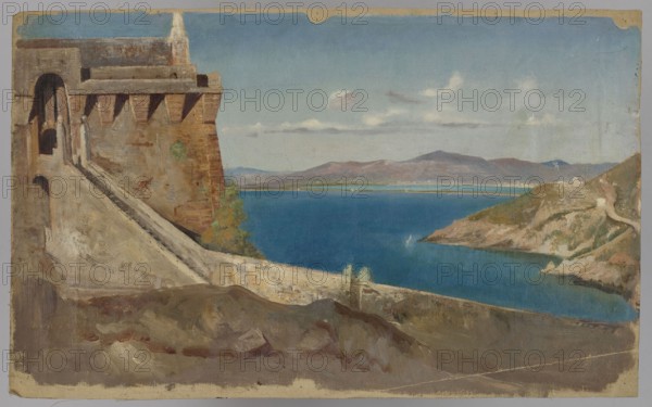 Building by the Sea, Pius Welonski 1849–1931, painter; deposits, 1st quarter of the 20th century; painting; height 56 cm, width 34 cm, A coastal scene showing a large stone fortress or wall on the left with an archway and sloping ramp, rendered in brown and beige tones; a rocky foreground in muted browns and grays; a vivid blue body of water stretching across the middle; a rocky headland on the right with earthy browns, greens, and beige cliffs; distant low mountains in washed purples and browns beneath a pale blue sky with a few soft white clouds; small areas of green vegetation near the wall and along the shoreline.