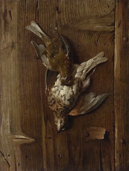 Dead Birds The Thrush and the Fieldfare, Jacques-Charles Oudry 1722/1723–1778, painting, 1768; French still life, hunting still life, trompe-l'oeil; subjects: birds; oil on panel, 37.7 × 26.2 cm., A group of two dead birds hangs upside down by a small loop against a wooden surface; one bird has mottled white and brown feathers with grayish wings and a darker speckled head, while the other bird has olive-green and brown plumage with lighter wing tips; the wooden background shows grain patterns and knots in shades of brown and tan with some darker streaks and a few small round fasteners.