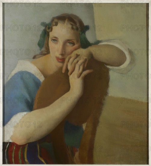 Portrait of a Wife, Jacek Mierzejewski 1883–1925, painter; 1919; interwar period, Poland. Contemporary painting in the Formist style Formists, 1917–1922. Subject: artist's wife; women's portrait. Painting; height 56.5 cm, width 51 cm., A painted portrait of a young woman leaning on the back of a wooden chair, with a pale face, pink lips, and light brown hair tied with green ribbons; she wears a blue garment with white trim and her exposed arms are pale; the chair back is brown and occupies the center foreground; the background shows muted beige and light gray tones and a floor area in warm tan; a few brightly colored striped cloths with red, green, blue, and yellow appear near the lower edge.