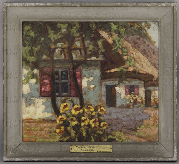 Polish Cottages, Jan Bohuszewicz 1878–1935, painter; contemporary painting; cottages; interwar period landscapes; 1929; Italy, — oil painting, 35 × 40 cm., A framed oil painting of a rustic cottage scene with a thatched roof, visible tree trunks and branches in the foreground, a cluster of bright yellow flowers near the base of the trees, and textured walls showing areas of pale blue and off-white. The windows have dark panes and reddish shutters, and there are additional small flowers near another doorway. The roof shows warm brown and tan tones, the ground and surrounding foliage include shades of green and brown, and the frame is a weathered gray with lighter worn edges.