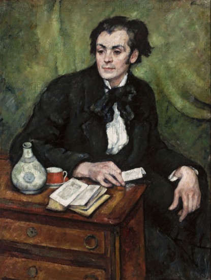 Portrait of Jan Rubczak, Kramsztyk, Roman 1885–1942 painter, ca. 1910, Poland; contemporary painting; portrait of artist Jan Rubczak 1884–1942; painting, height 115 cm, width 88 cm., A seated person with dark hair and pale skin wears a black coat and a white shirt with a dark bow at the neck, positioned against a green background; the person’s expression is neutral and gaze is directed slightly to the side. In front of them is a wooden table with a warm brown tone, on which lie a few open books, a light-colored round bottle with subtle blue-gray markings, and a small red cup; one hand rests on the table near the books while the other hand hangs over the table edge. Visible colors include black, white, green, brown, red, pale skin tones, and muted blue-gray.