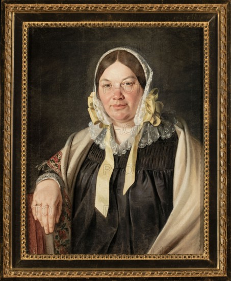 Portrait of Aleksandra Bebnowska, née Cybulska, the painter's mother-in-law; Jan Chrucki 1810–1885, painter; ca. 1845; painting; female portrait, half-length, seated, full-face; Biedermeier style; scarves, bonnets, wedding rings; iconography: Aleksandra Bebnowska fl. ca. 1845., A framed painted portrait of a woman shown from the waist up against a dark background, wearing a white lace cap with yellow ribbons and a dark dress with gathered bodice details, a light-colored shawl draped over her shoulders, and a patterned sleeve visible on one arm; her hand rests on a cushioned armrest and she wears a ring. The frame is ornate and gold with decorative beading and rope-like trim. Visible colors include black, white, yellow, beige, gold, brown, red, green, and pale skin tones.